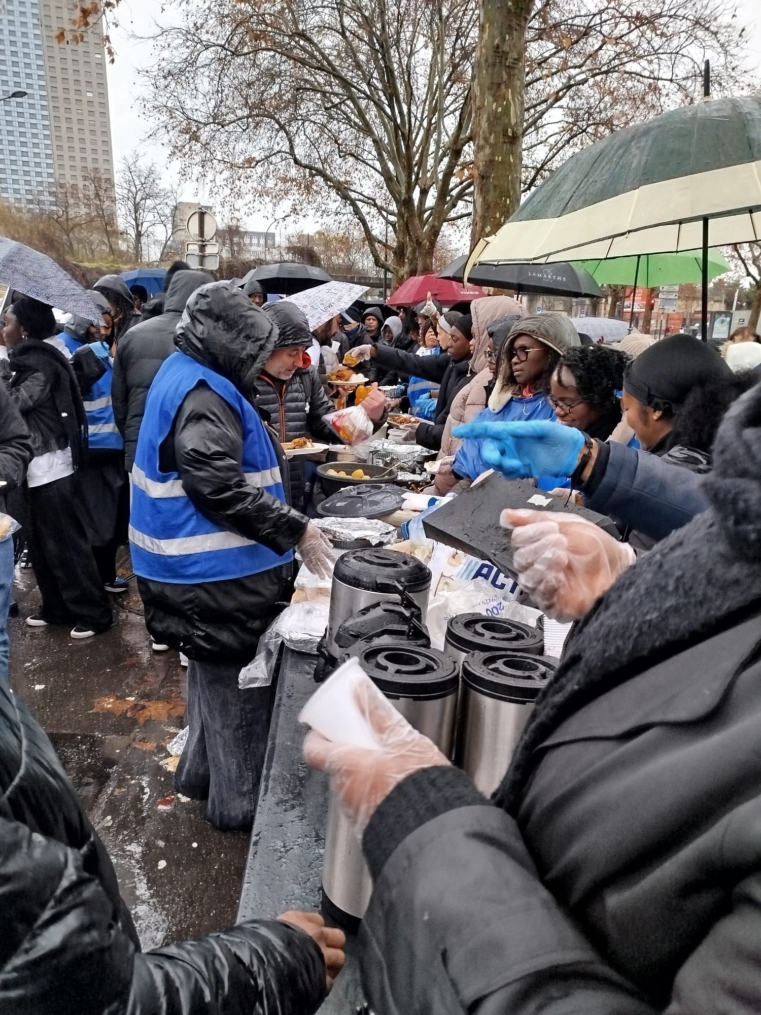Des bénévoles en gilet bleu servent des boissons chaudes au stand de la Confrérie, Porte de la Villette