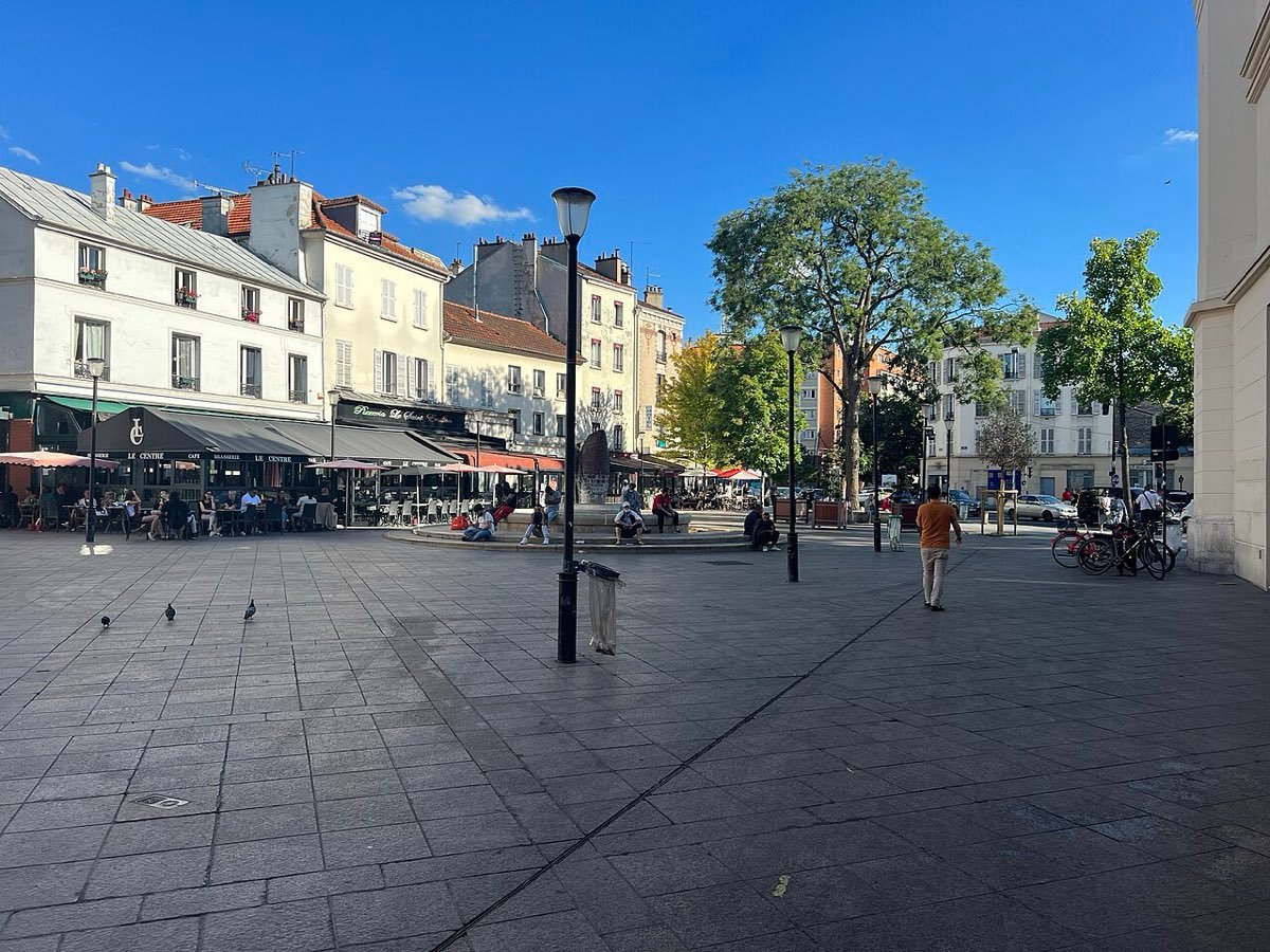 La place de la Mairie d'Aubervilliers, pavée, avec ses terrasses de café et ses arbres