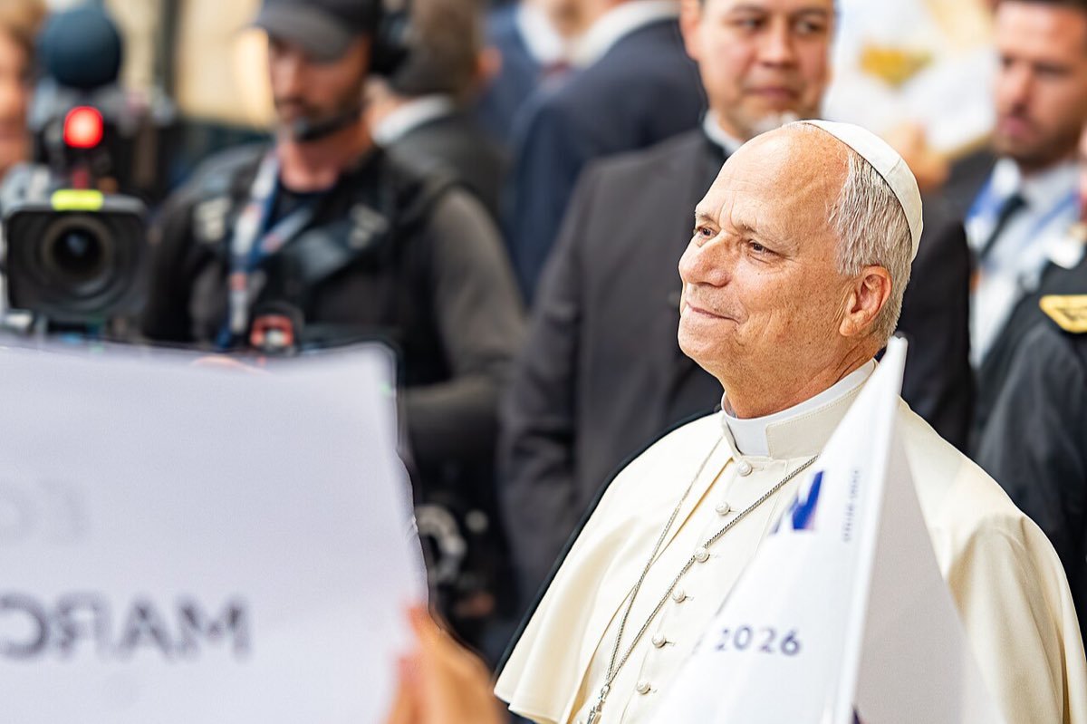 Le pape Léon XIV souriant, en soutane blanche, à Metz le 28 septembre 2026, un fanion marqué 2026 au premier plan