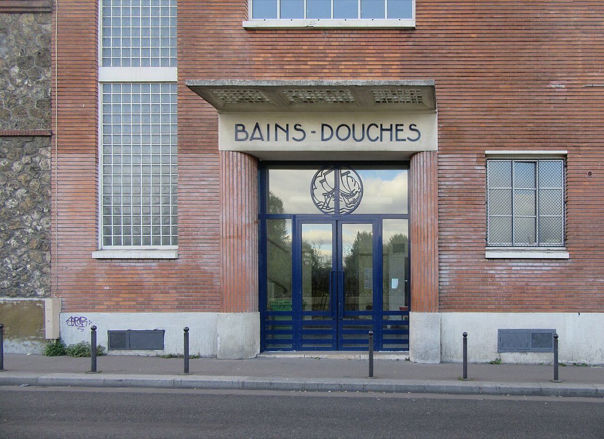 Façade en briques des bains-douches municipaux de la rue Rouvet, à Paris 19e, avec l'inscription Bains-Douches au-dessus de la porte bleue