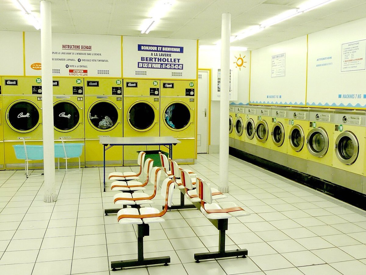 Intérieur d'une laverie automatique à Paris : machines à laver jaunes alignées contre les murs et sièges au centre