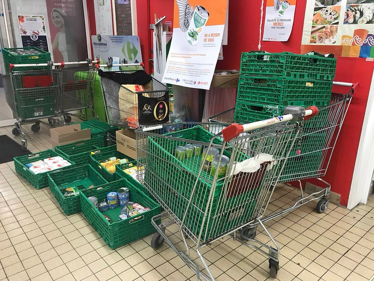 Chariots et cagettes vertes remplis de conserves à la sortie d'un supermarché lors d'une collecte alimentaire