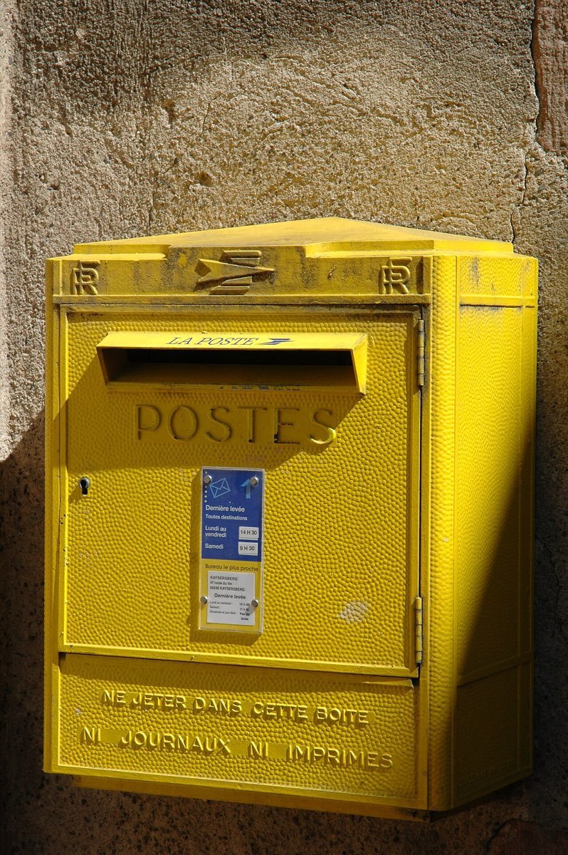 Une boîte aux lettres jaune de La Poste fixée sur un mur de pierre
